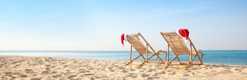 Sun loungers with Santa's hats on beach, banner design. Christmas vacation