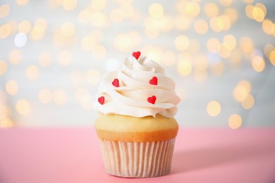 Tasty cupcake for Valentine's Day on pink table against blurred lights