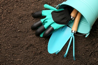Overturned bucket with gardening tools and gloves on fresh soil, flat lay. Space for text