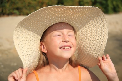 Smiling little girl in stylish hat on sunny day. Beach holiday