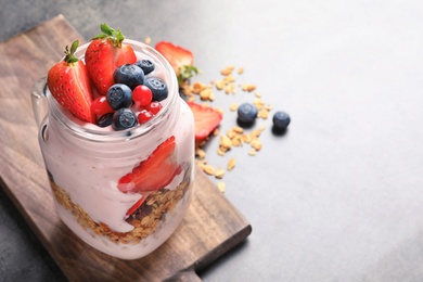 Photo of Mason jar with yogurt, berries and granola on table