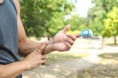 Young man checking pulse with medical device after training, closeup