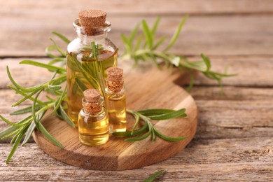 Photo of Aromatic essential oils in bottles and rosemary on wooden table, closeup. Space for text