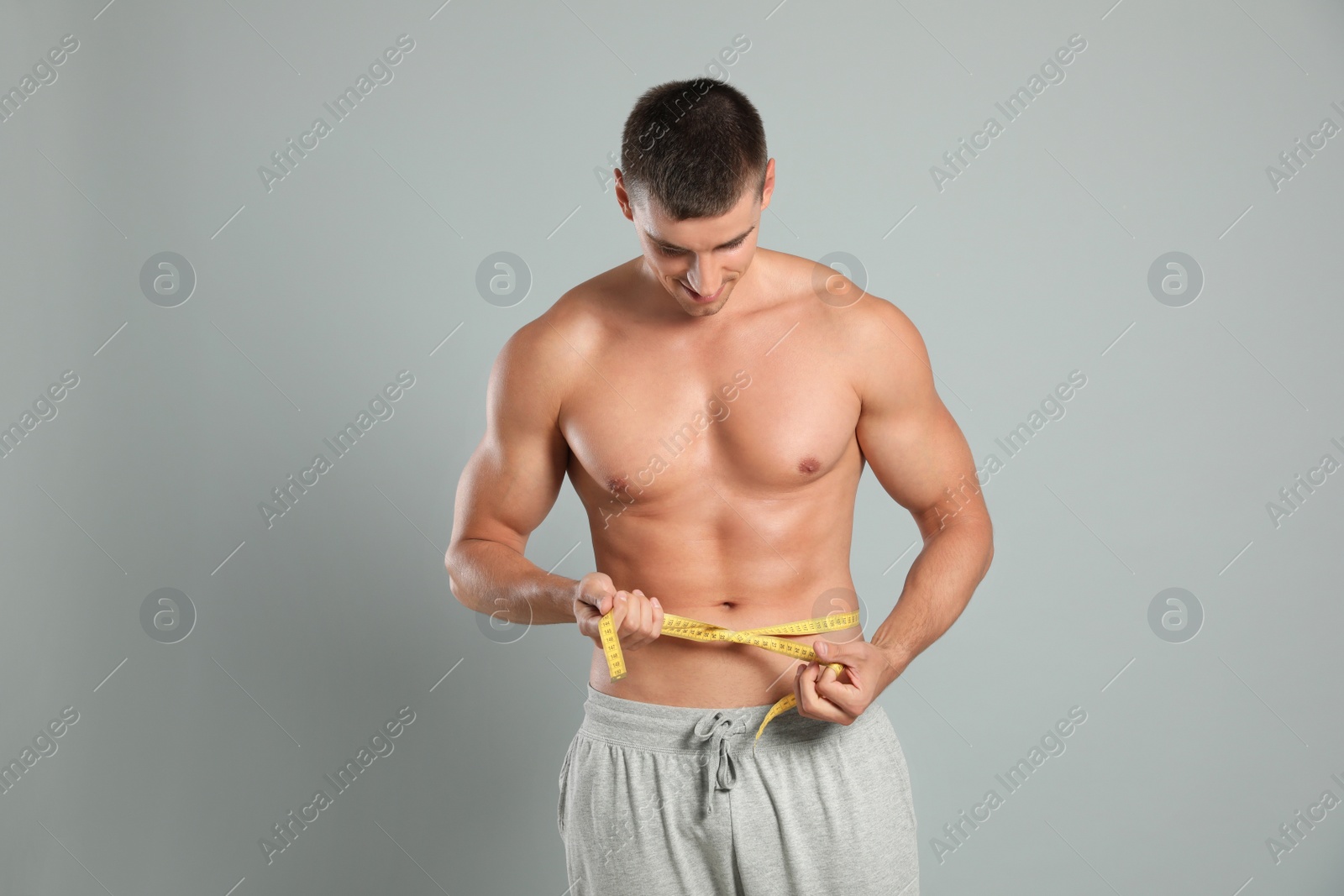 Photo of Young man with slim body using measuring tape on grey background