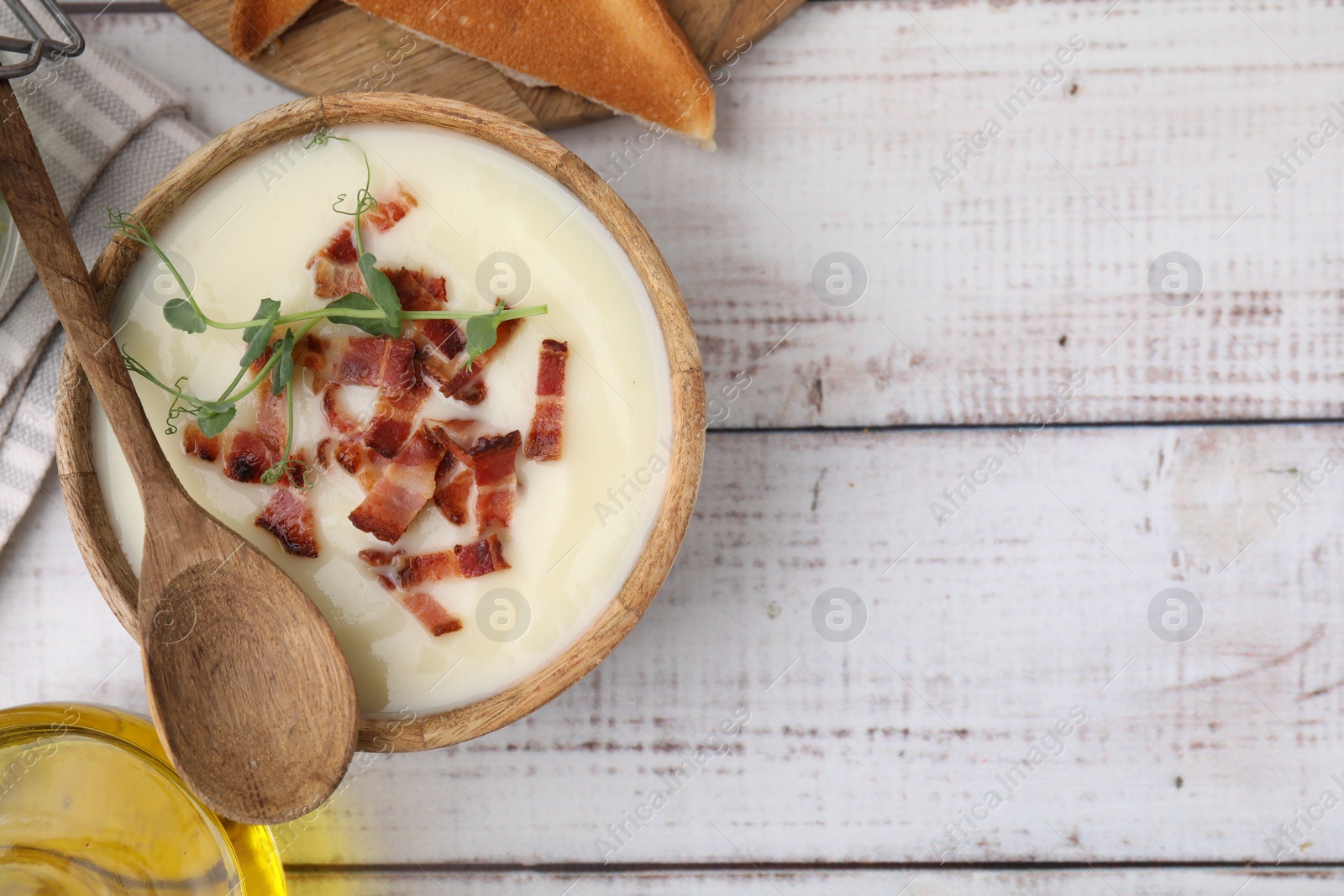 Photo of Delicious potato soup with bacon and microgreens in bowl served on wooden table, flat lay. Space for text