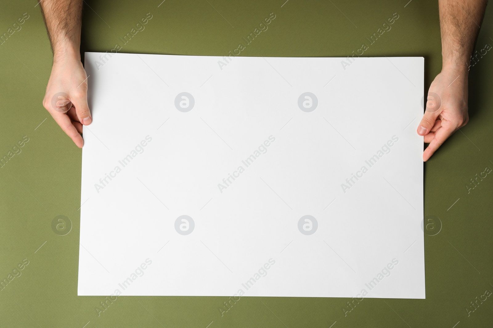 Photo of Man with empty sheet of paper on olive background, top view. Mockup for design