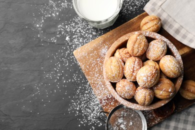 Photo of Delicious nut shaped cookies with powdered sugar and milk on black table, flat lay. Space for text