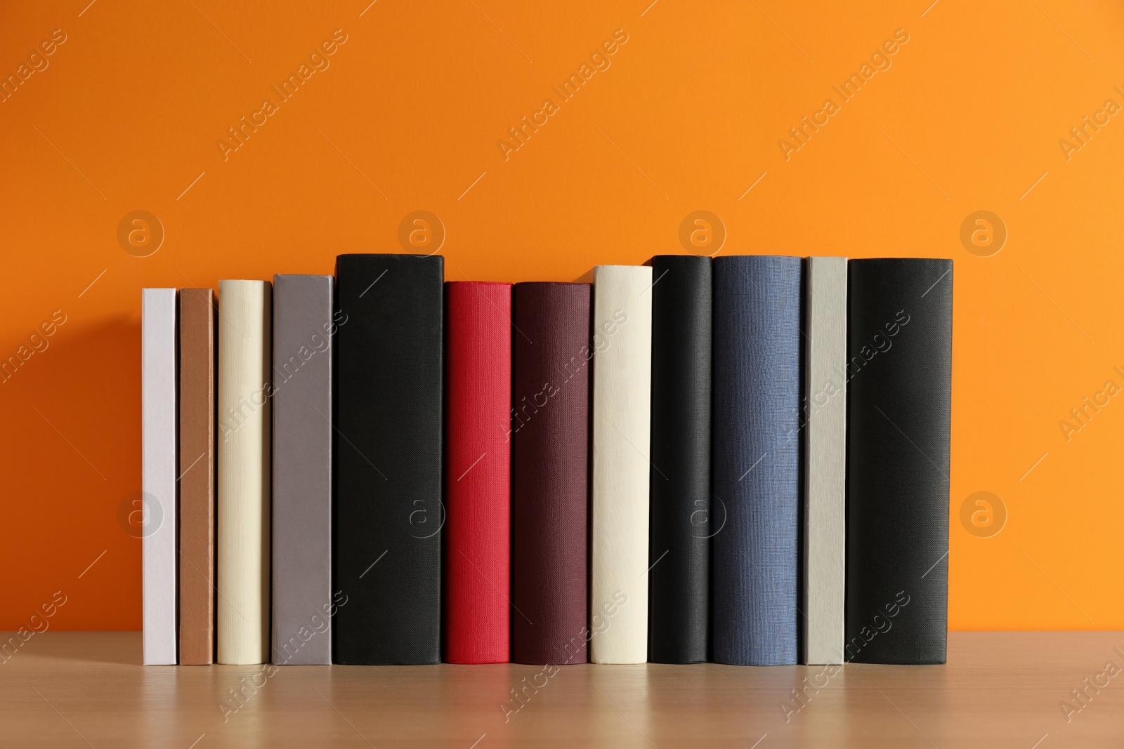 Photo of Many books on wooden table near orange wall