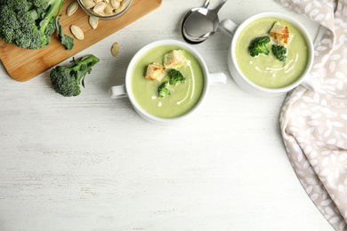 Photo of Delicious broccoli cream soup with croutons served on white wooden table, flat lay. Space for text