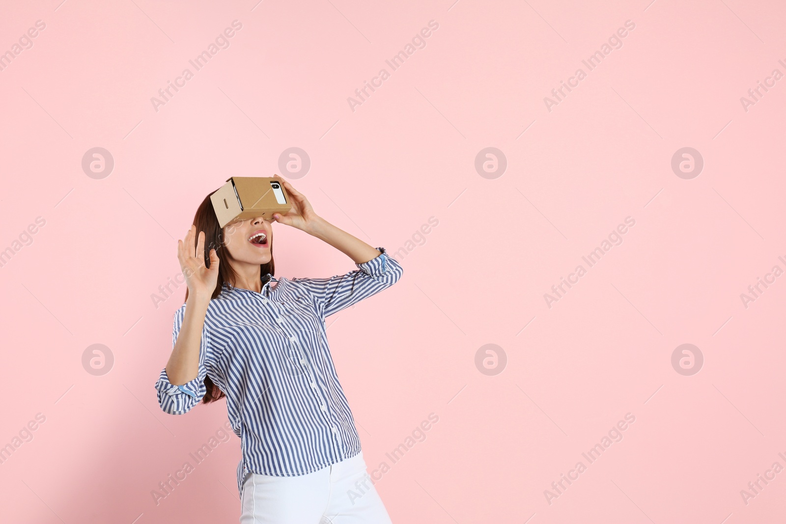 Photo of Young woman using cardboard virtual reality headset on color background. Space for text