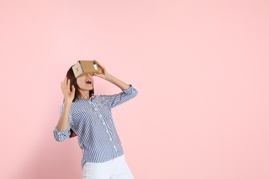 Young woman using cardboard virtual reality headset on color background. Space for text