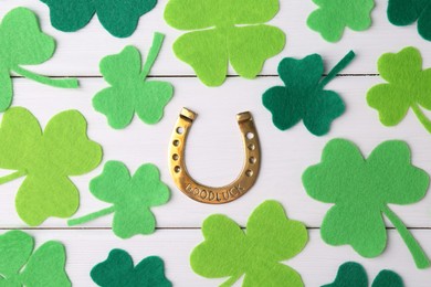 St. Patrick's day. Golden horseshoe and green decorative clover leaves on white wooden table, flat lay