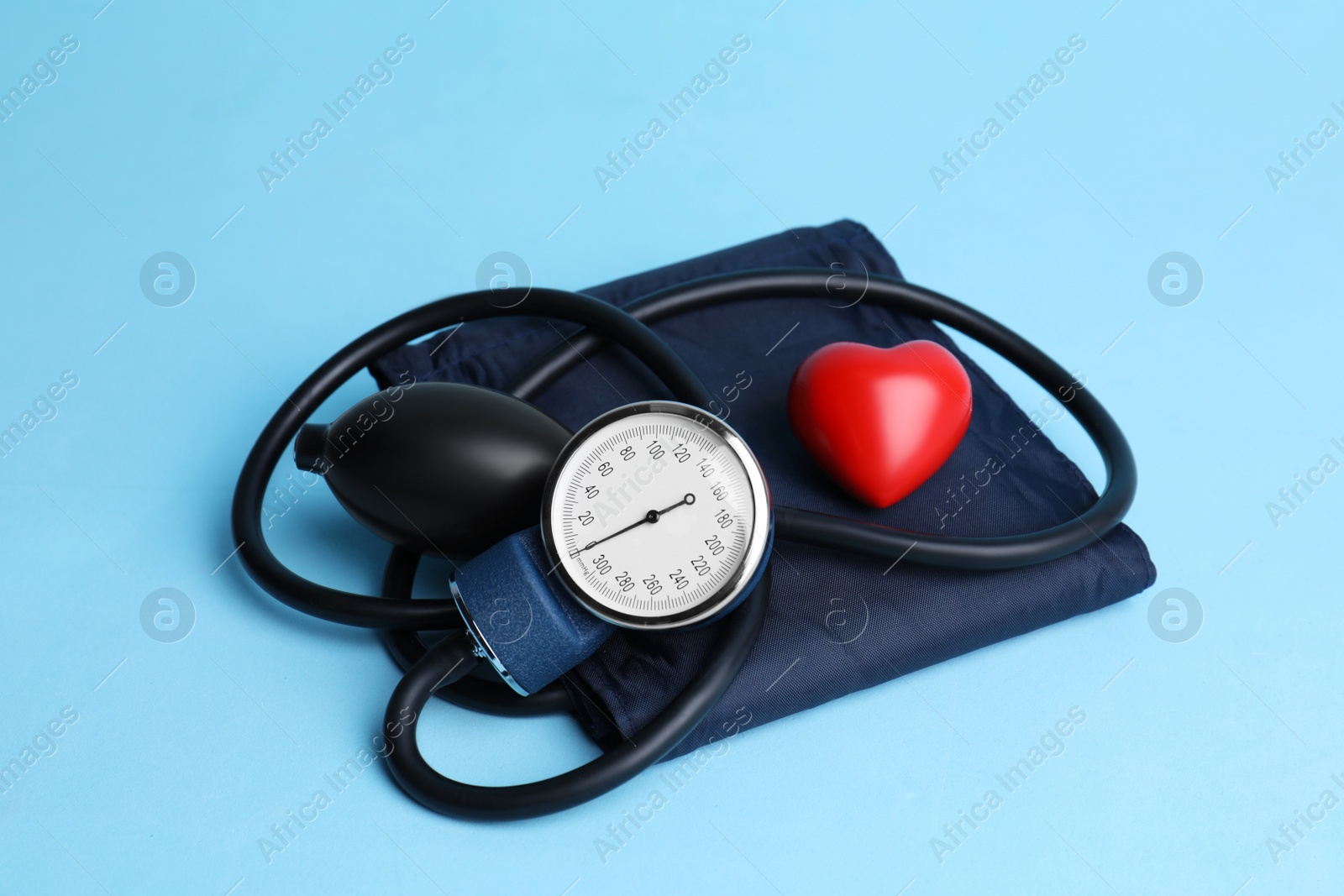 Photo of Blood pressure meter and toy heart on light blue background