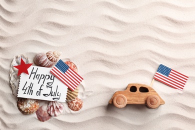 Photo of Flat lay composition with greeting card, USA flags and wooden car on sand. Happy Independence Day