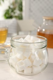 Photo of Glass jar of refined sugar cubes on white table