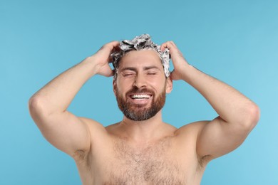 Happy man washing his hair with shampoo on light blue background