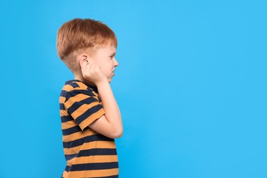 Photo of Little boy suffering from ear pain on light blue background. Space for text