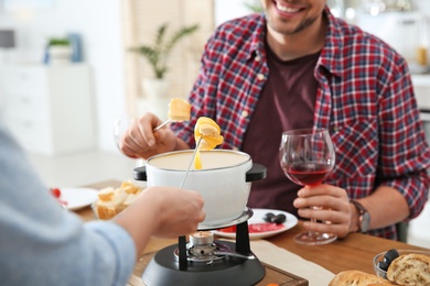 Photo of Happy couple enjoying fondue dinner at home, closeup