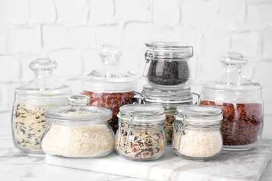 Photo of Brown and polished rice in jars on white marble table