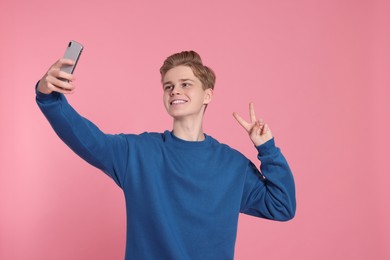Photo of Teenage boy taking selfie on pink background