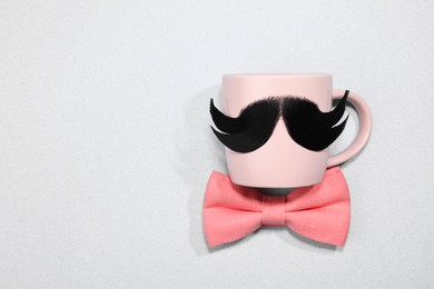 Photo of Man's face made of artificial mustache, bow tie and glasses on light grey background, top view. Space for text
