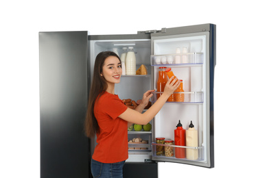 Young woman taking juice out of refrigerator on white background