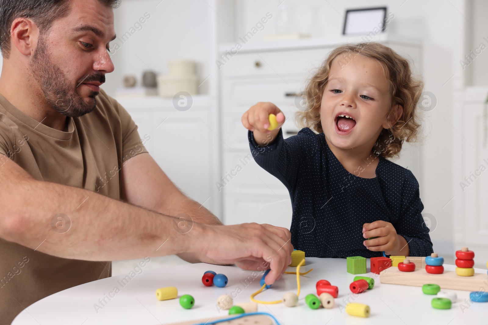 Photo of Motor skills development. Father and daughter playing with wooden pieces and strings for threading activity at table indoors