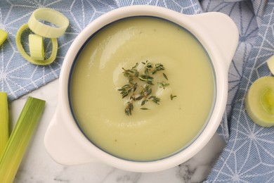 Photo of Tasty leek soup in bowl on white marble table, flat lay