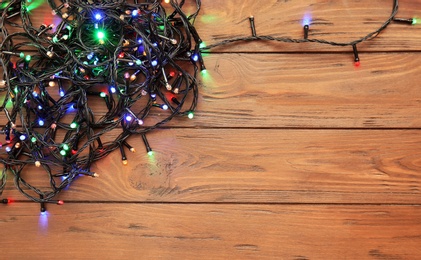 Glowing Christmas lights on wooden background, top view