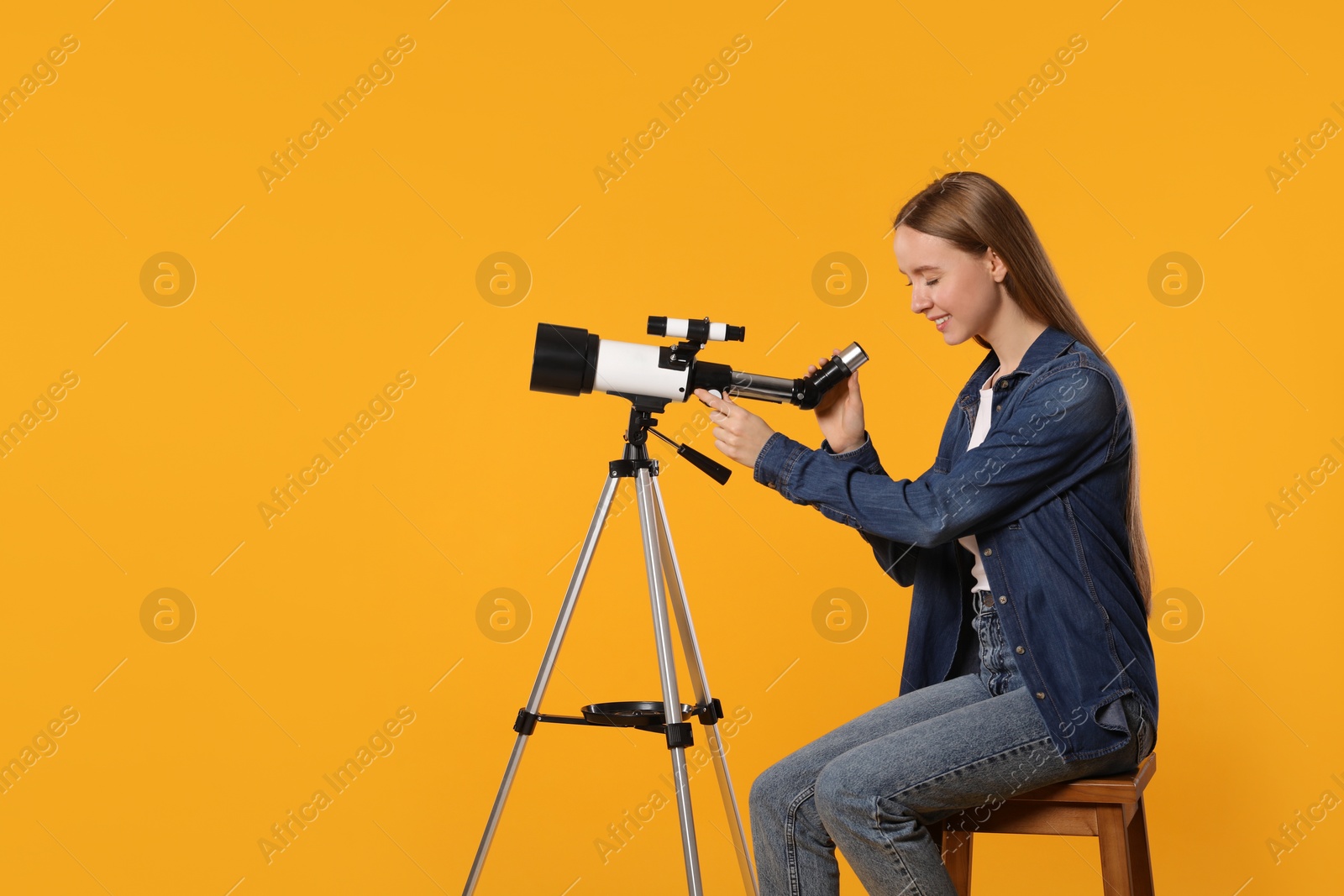 Photo of Young astronomer looking at stars through telescope on orange background, space for text