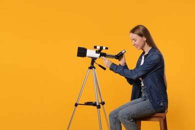 Young astronomer looking at stars through telescope on orange background, space for text