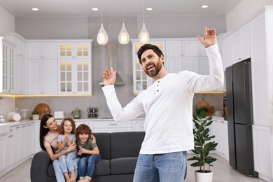 Photo of Happy family having fun at home. Father dancing while his relatives resting on sofa