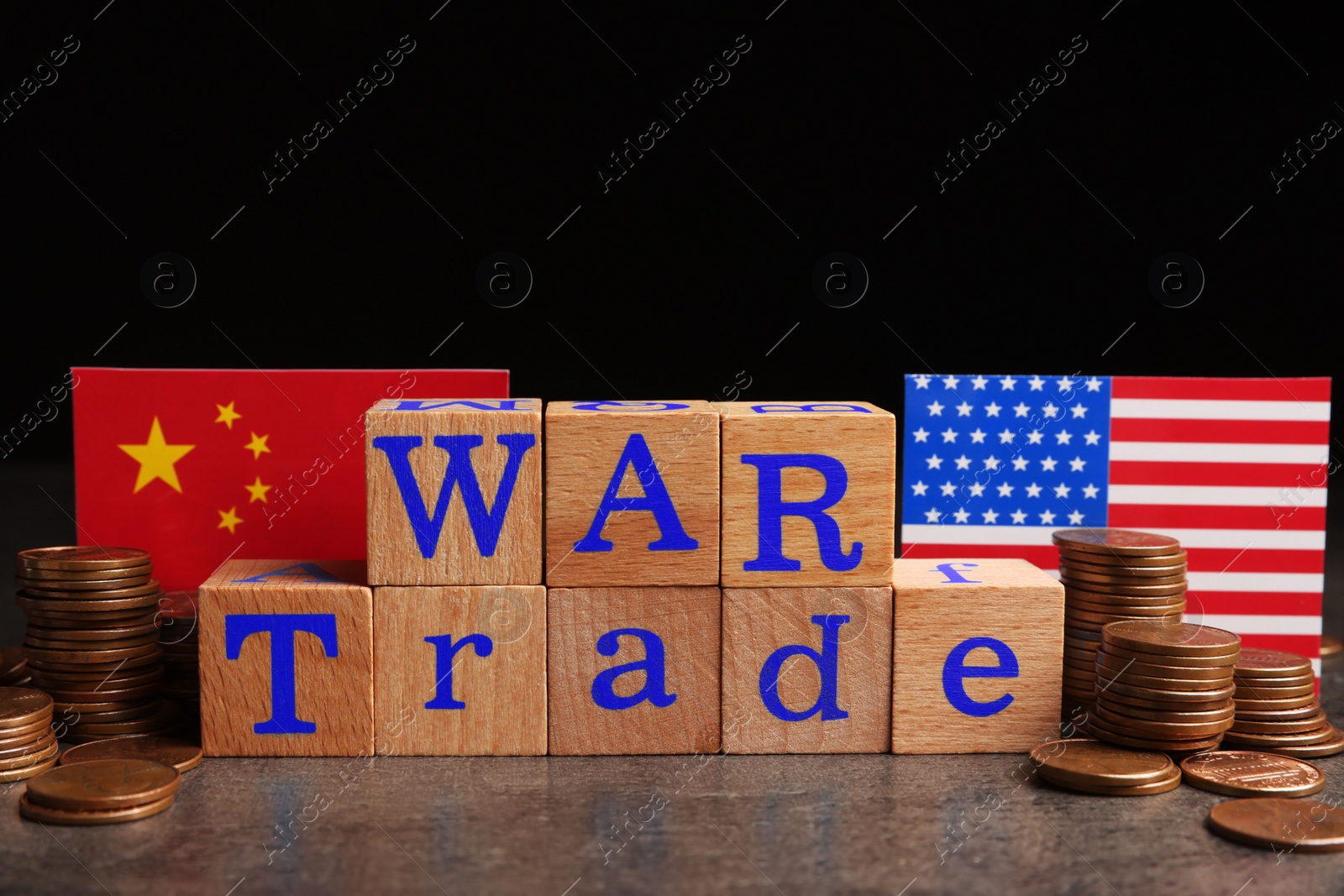 Photo of Words War Trade made of wooden cubes, American and Chinese flags with coins on grey table against black background