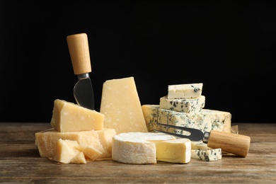 Photo of Different sorts of cheese, fork and knife on wooden table against black background