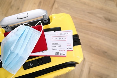 Photo of Passport with protective face mask and tickets on yellow suitcase, above view. Travel during quarantine