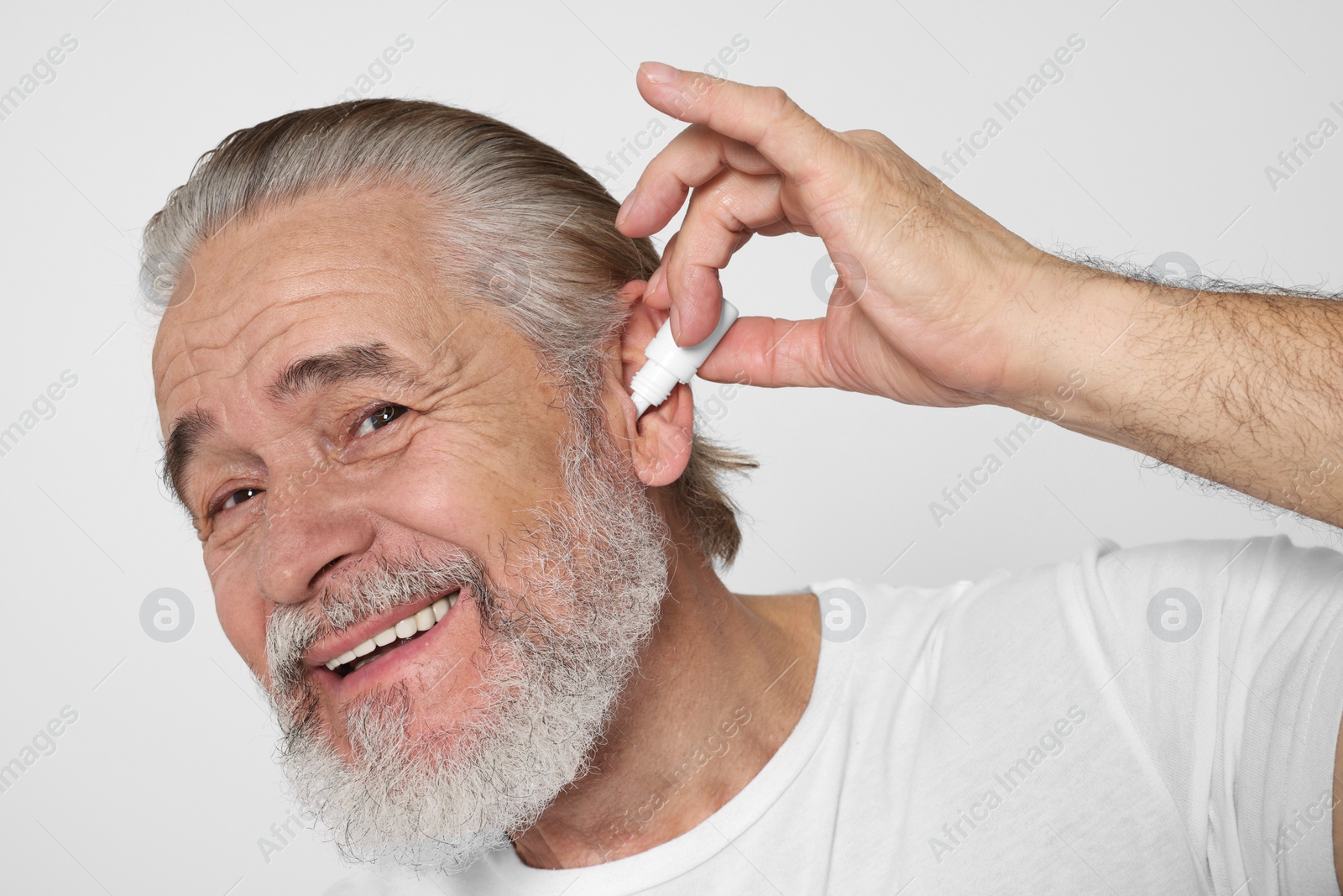 Photo of Senior man using ear drops on white background