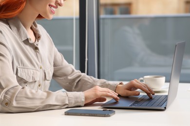 Photo of Woman working with laptop at white desk in office, closeup