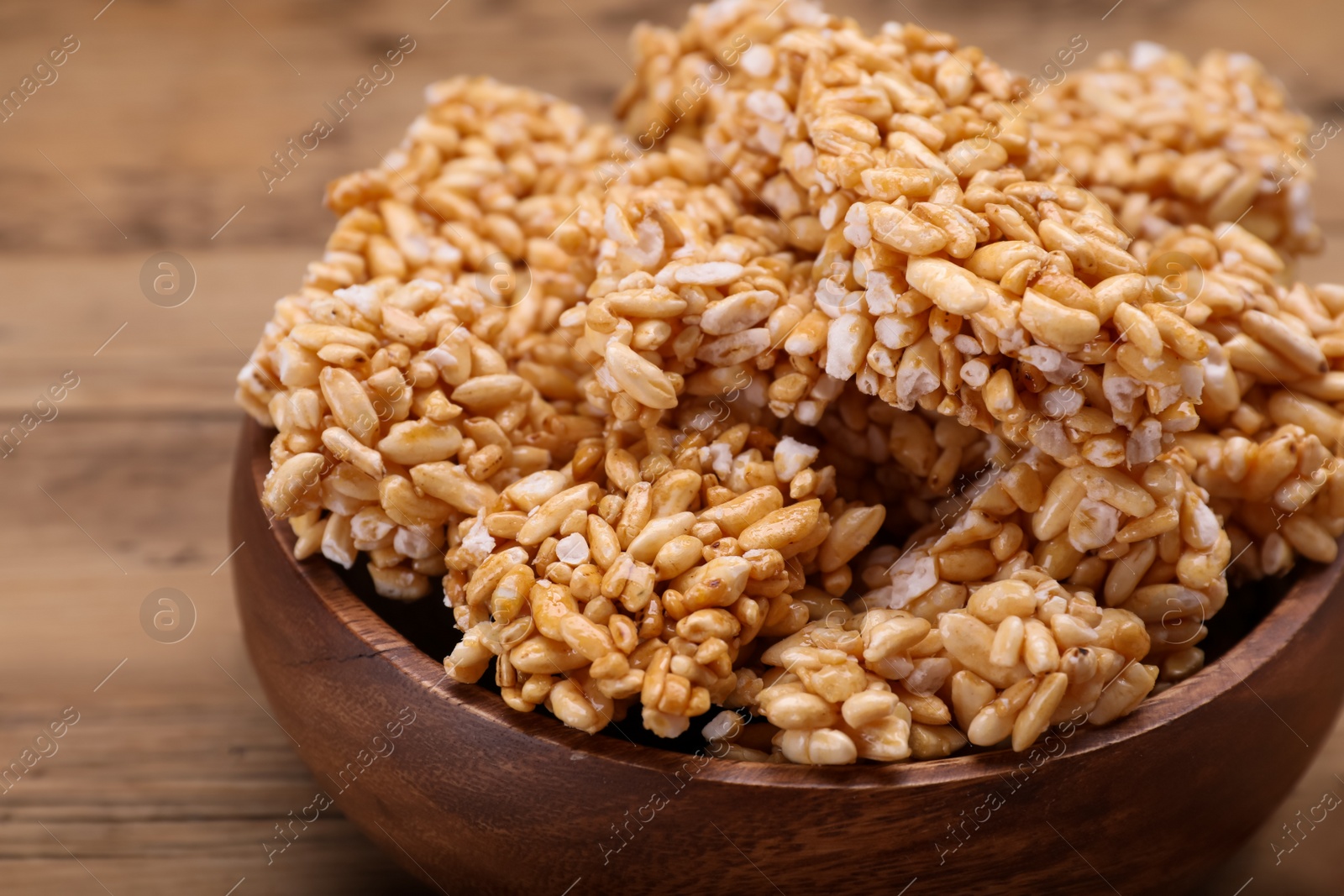 Photo of Bowl of puffed rice pieces (kozinaki) on wooden table, closeup