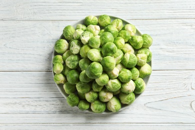 Photo of Plate with fresh Brussels sprouts on wooden background, top view