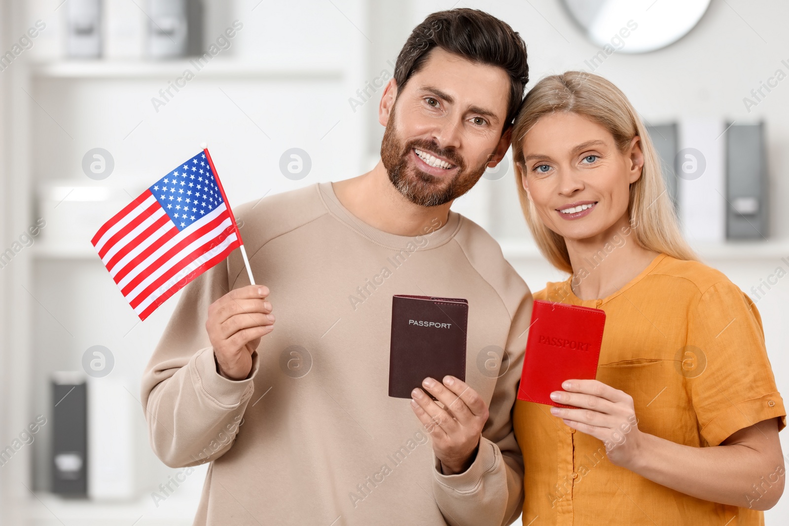 Photo of Immigration. Happy couple with passports and American flag indoors