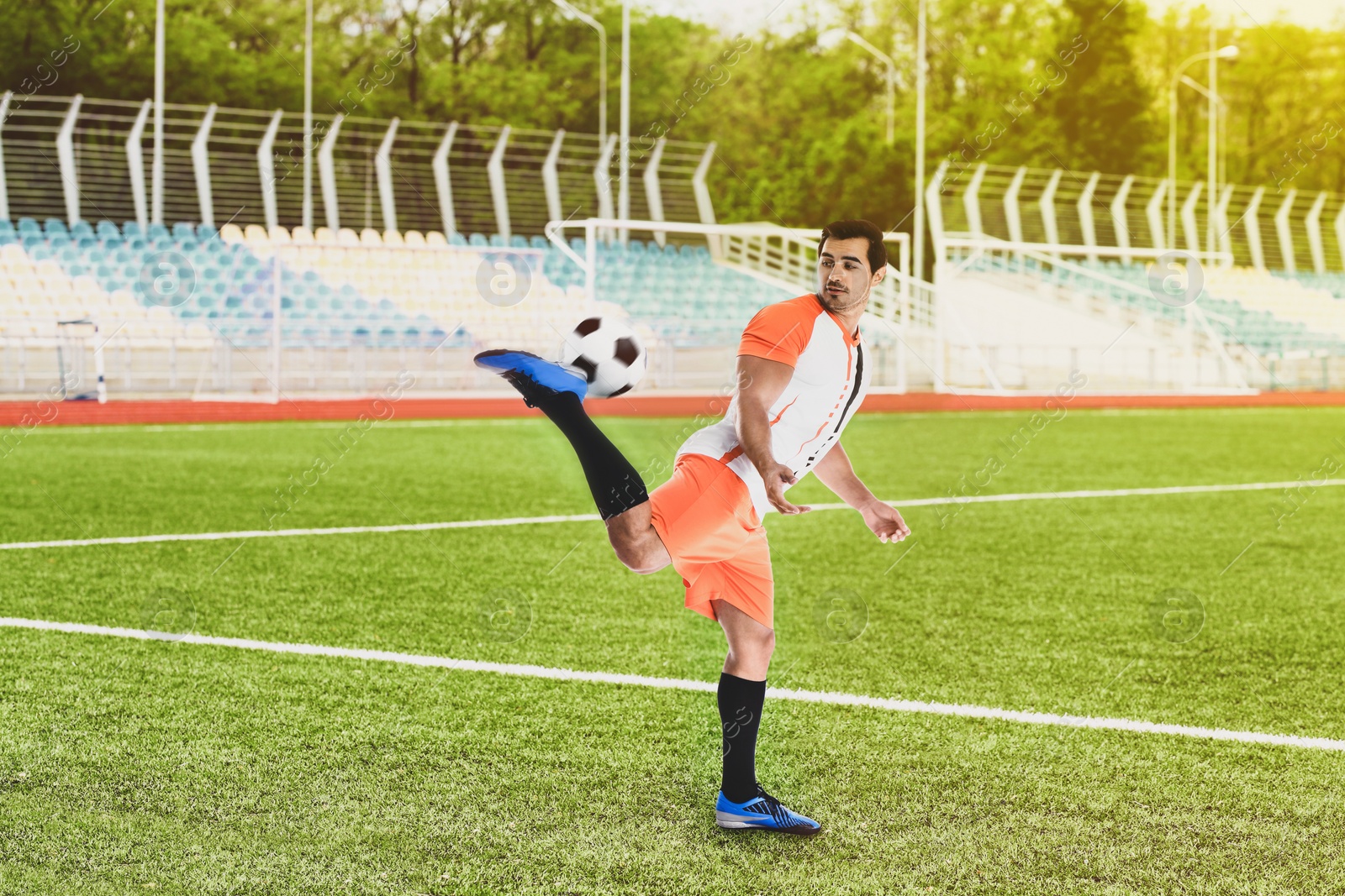 Image of Young man in uniform playing football at stadium