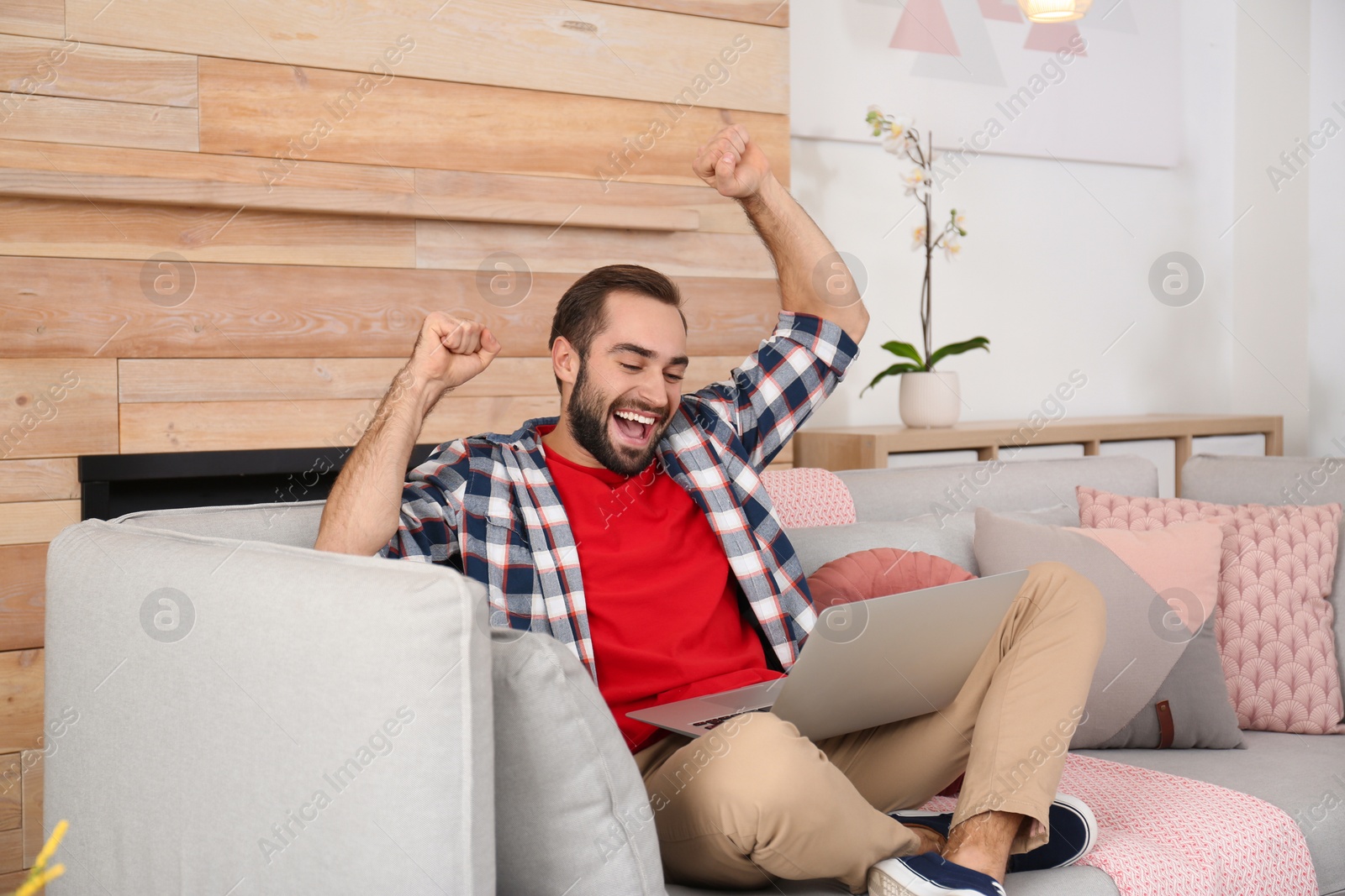 Photo of Emotional young man with laptop celebrating victory on sofa at home