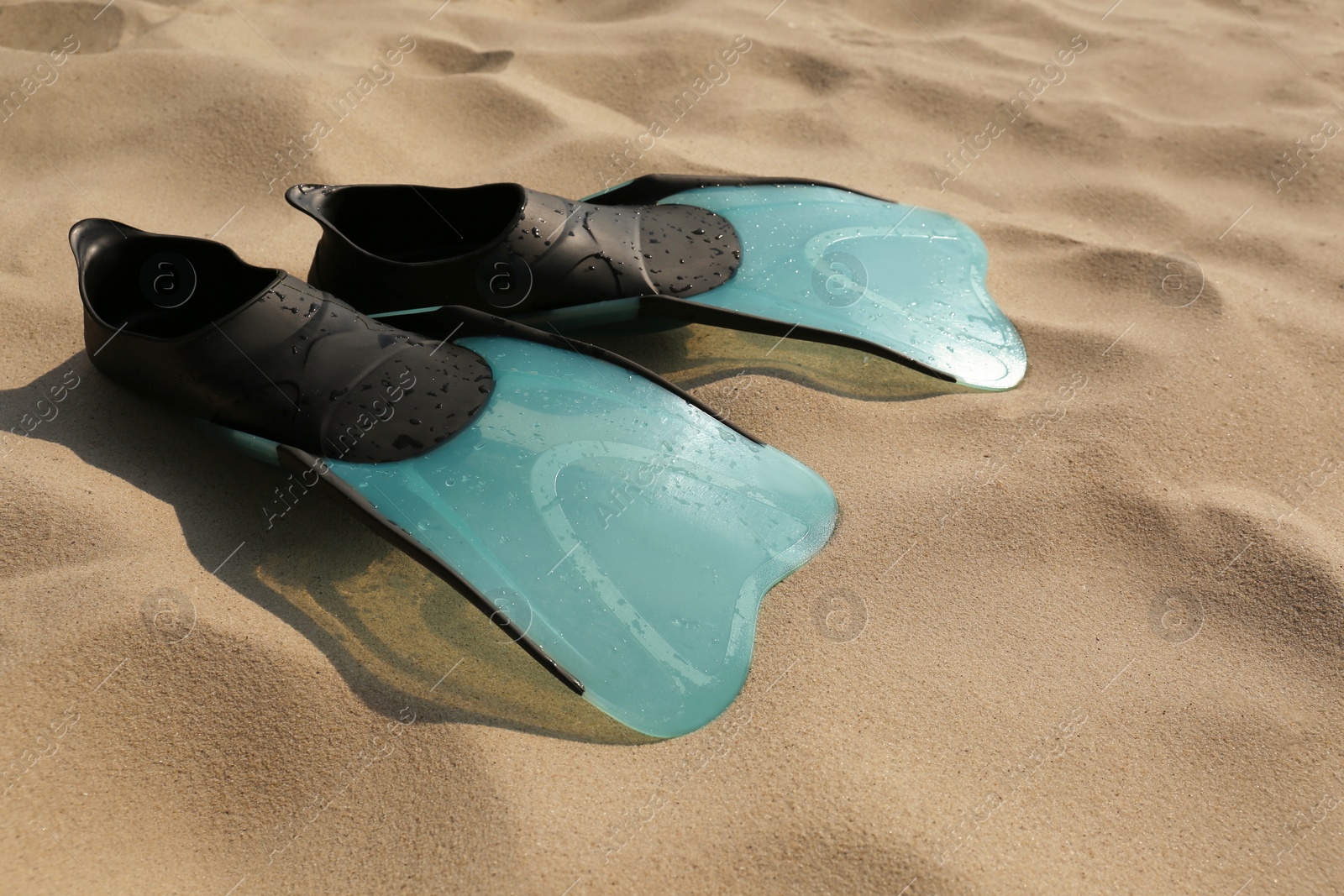 Photo of Pair of turquoise flippers with water drops on sand, closeup