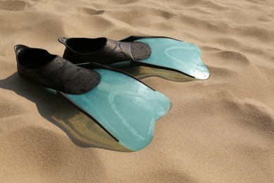 Photo of Pair of turquoise flippers with water drops on sand, closeup