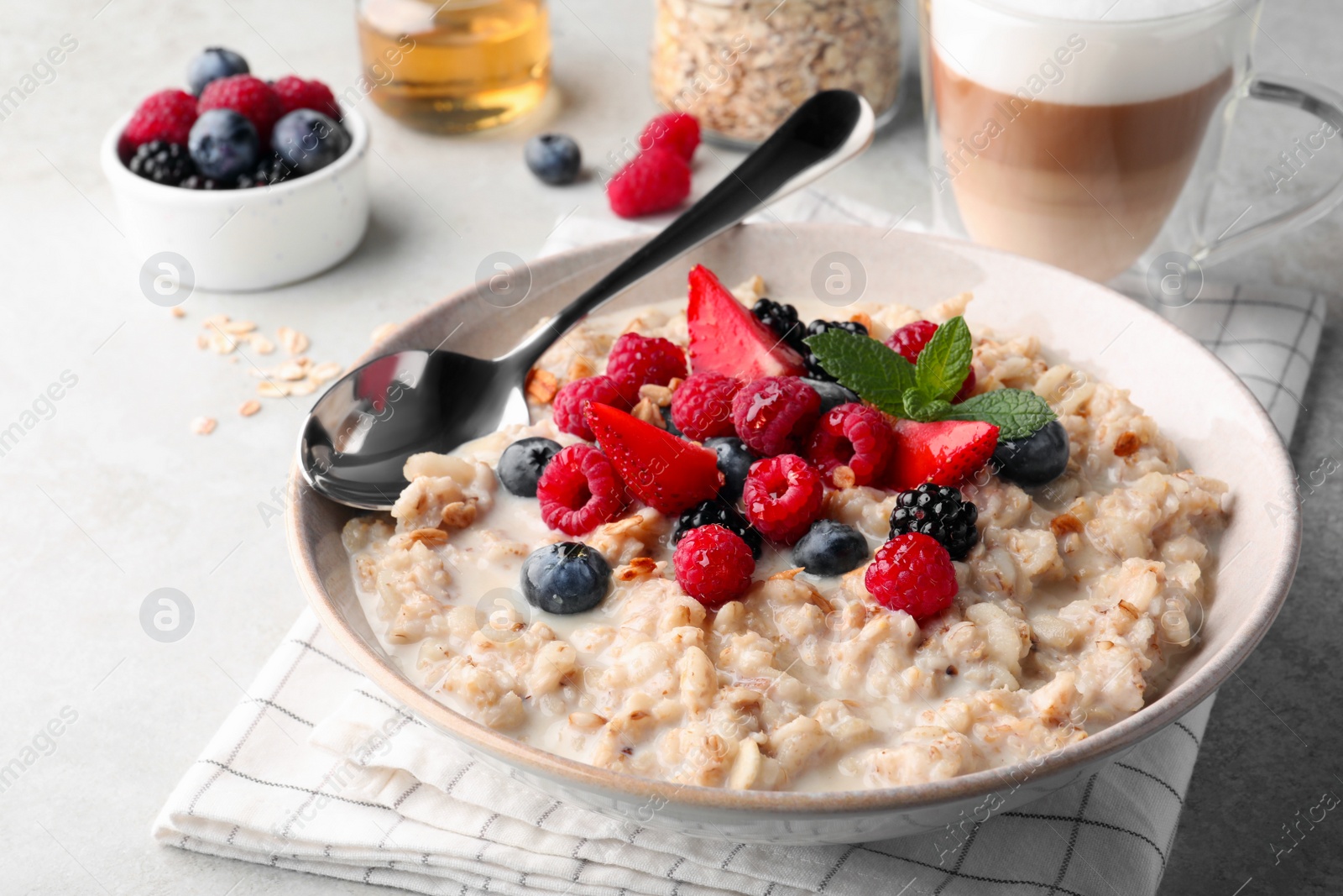 Photo of Bowl of oatmeal porridge served with berries on light grey table, closeup