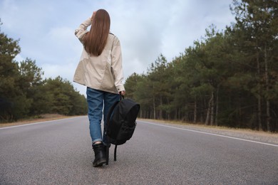 Young woman with backpack going along road near forest, back view