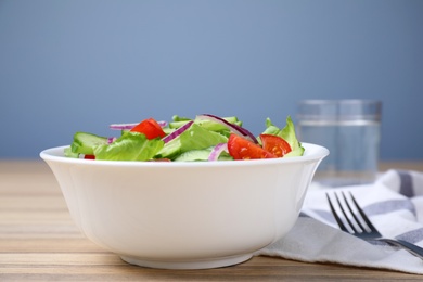 Photo of Bowl of tasty salad with cucumber, tomato and lettuce on table