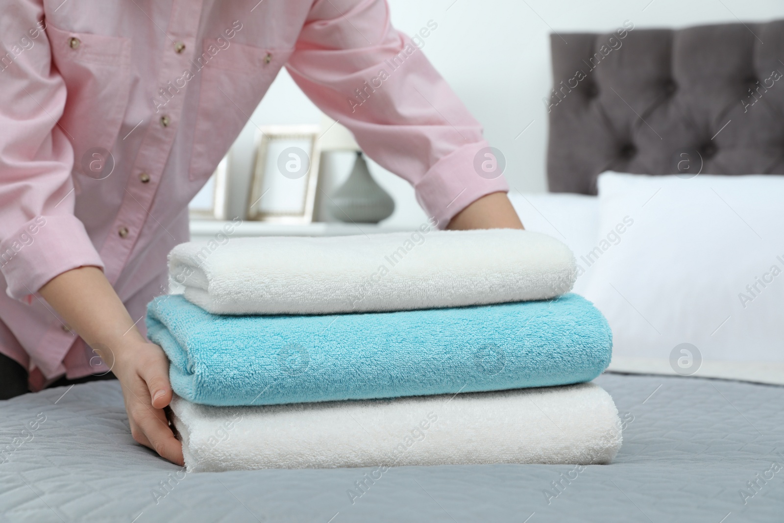 Photo of Woman putting stack of clean towels on bed
