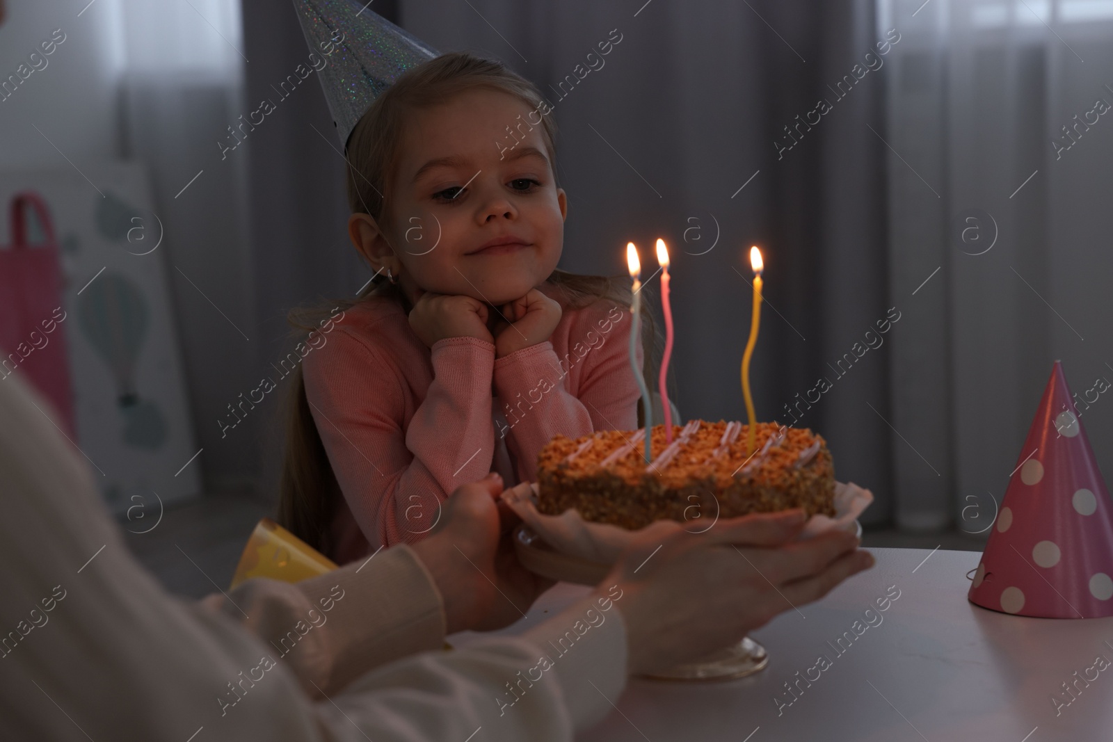 Photo of Birthday celebration. Mother holding tasty cake with burning candles near her daughter indoors