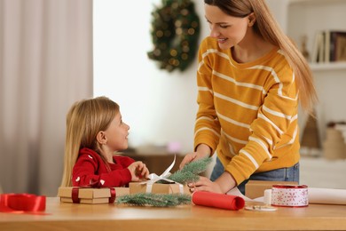Photo of Christmas presents wrapping. Mother and her little daughter decorating gift box with fir tree branch at home